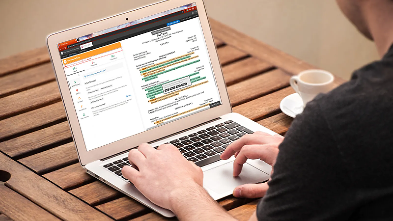 A student sits at a wooden table working on their resume through the VMock interface.