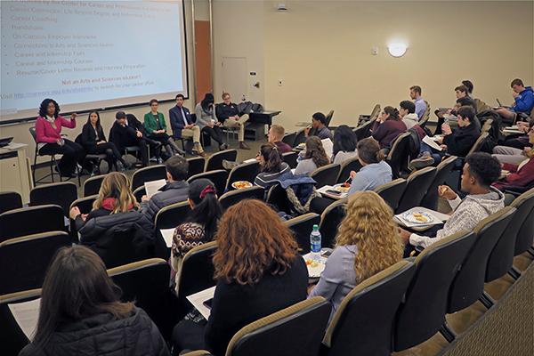 A large group of students in a lecture hall listen to a panel of professionals